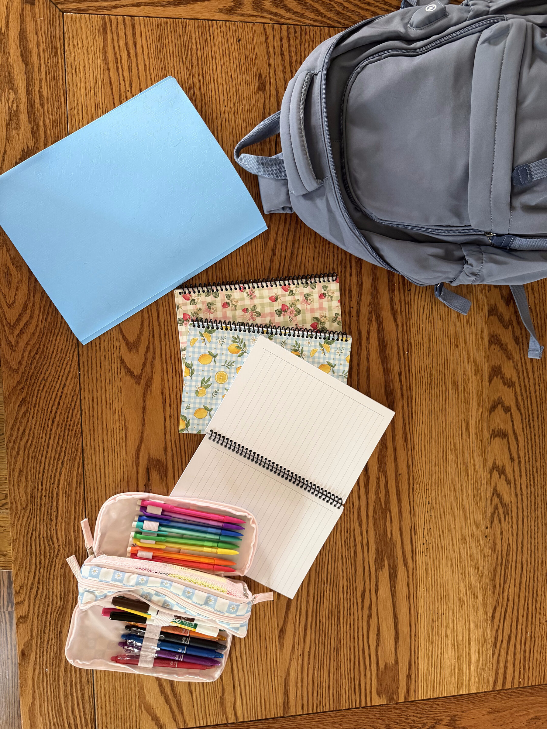 A folder, notebooks, pencil case, and backpack laid out and ready to go on the floor