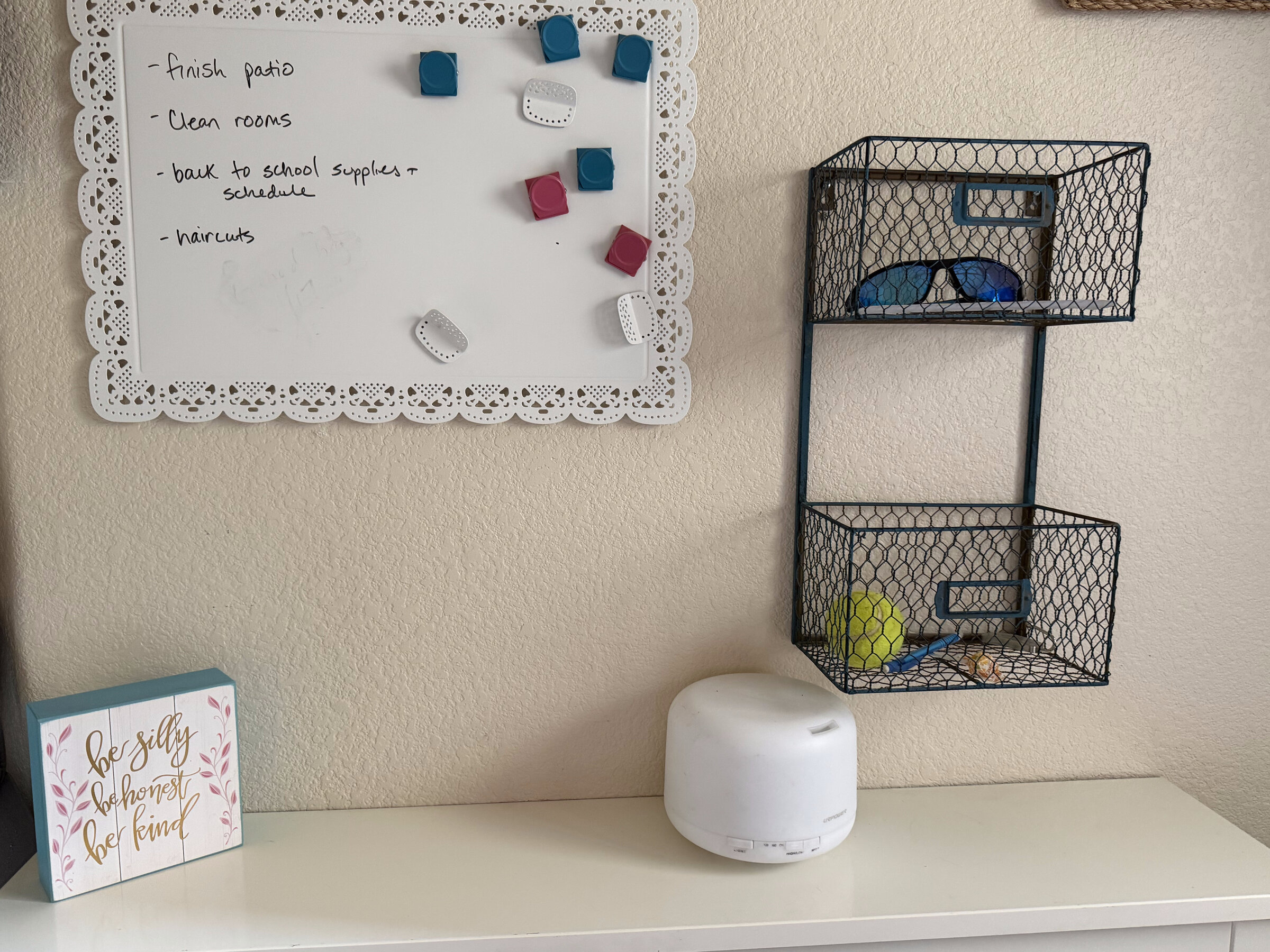 A dry-erase to-do board and a wall-mounted wire basket holding sunglasses and everyday small stuff