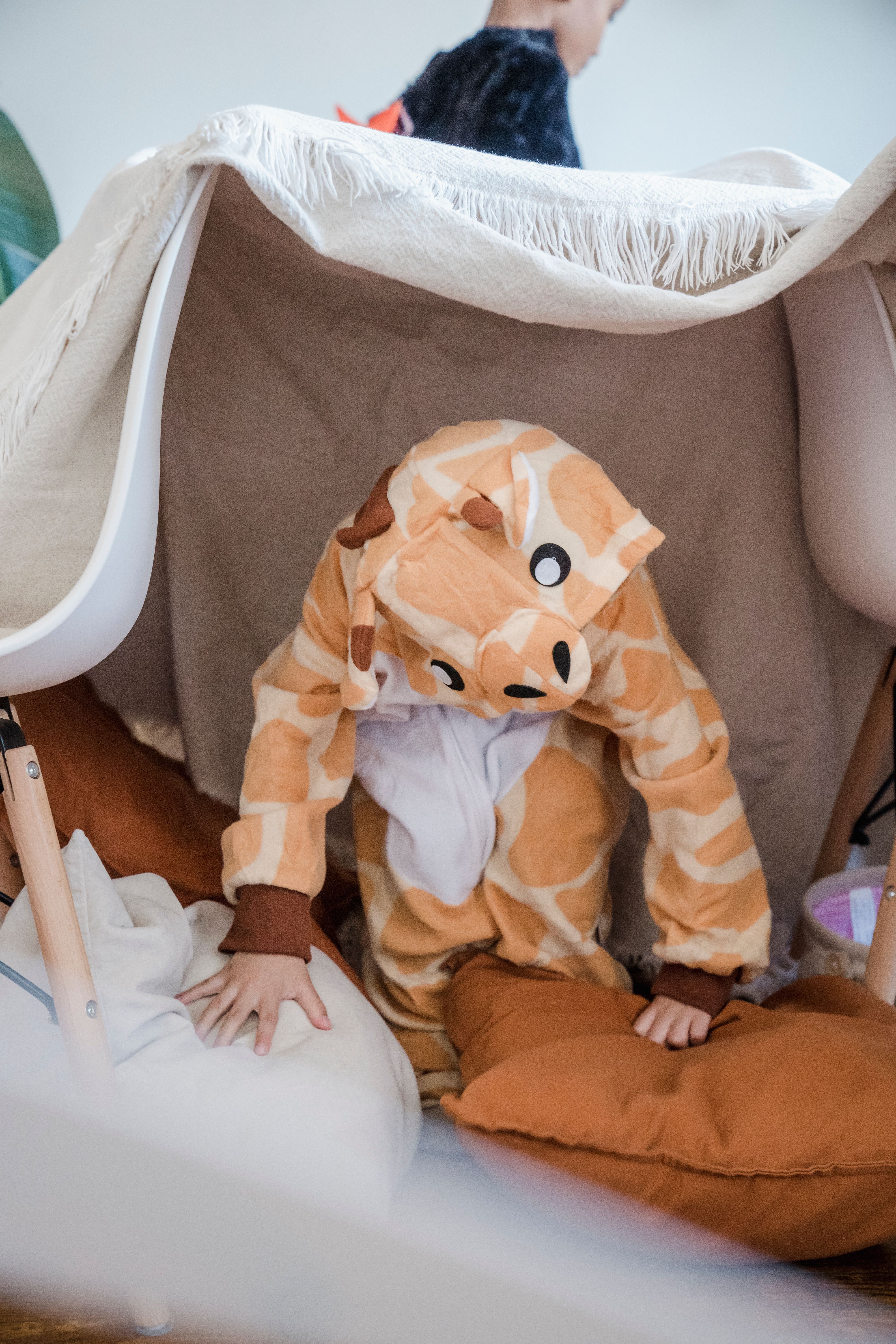 Child in a giraffe costume playing inside a blanket fort