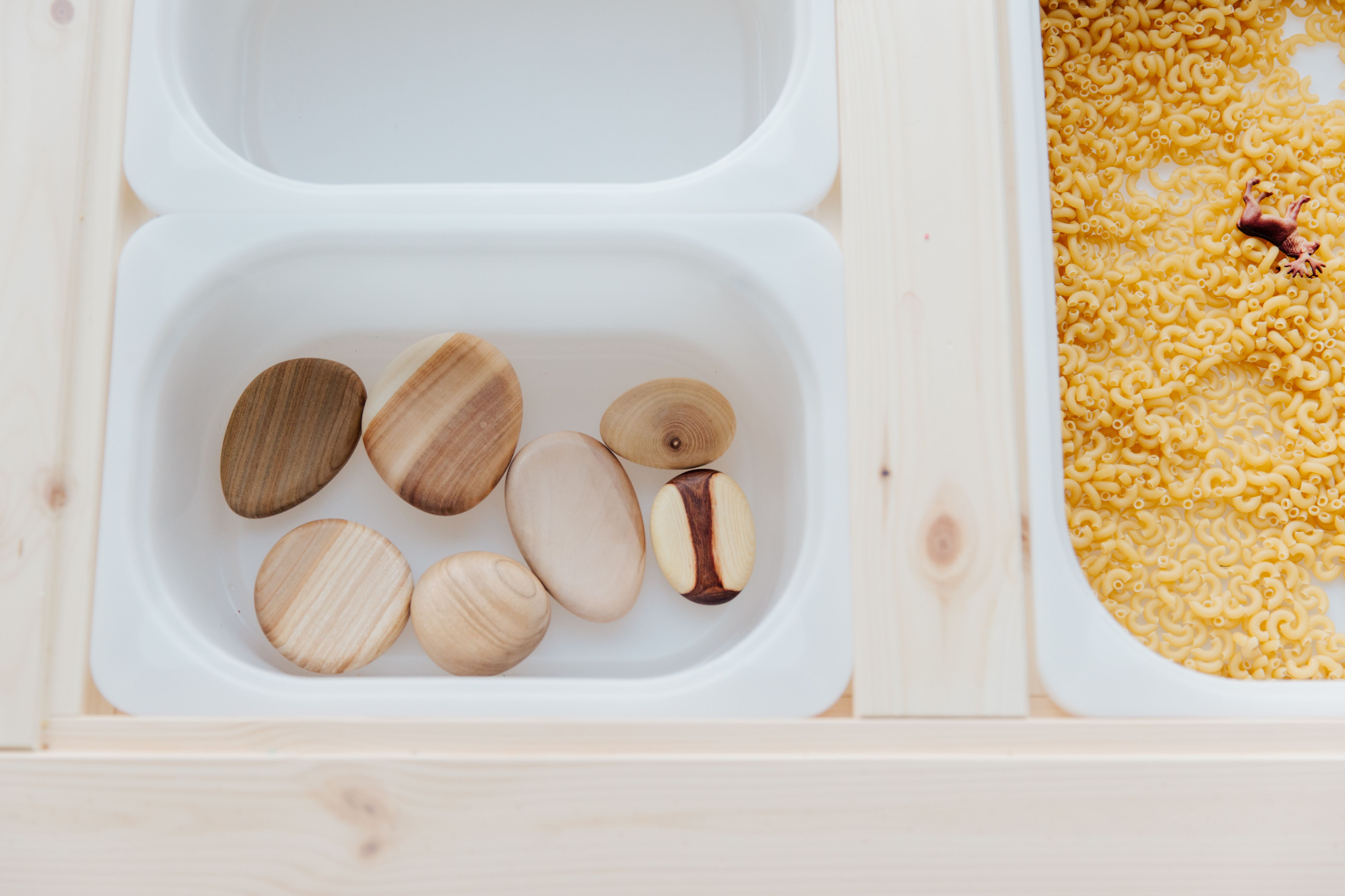 Plastic containers filled with dried pasta and stones, set up for sensory bin play