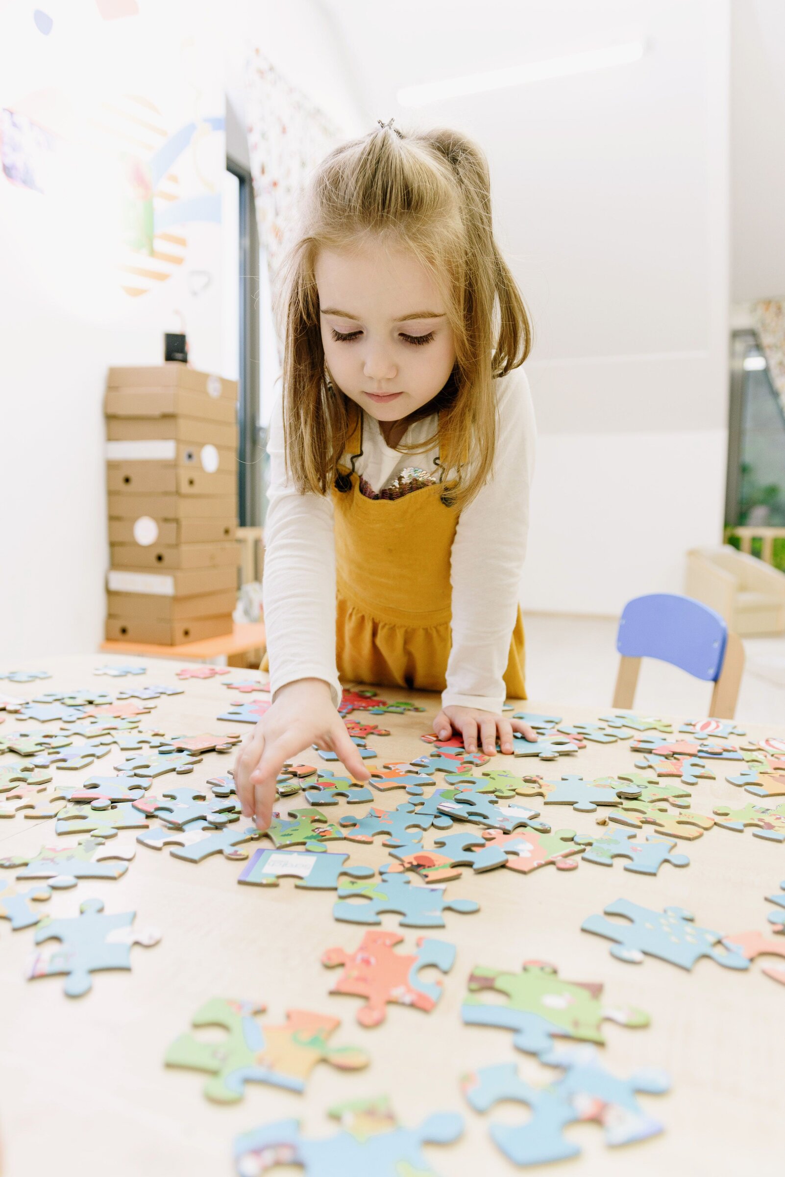 A young child leaning over a table covered in scattered jigsaw puzzle pieces