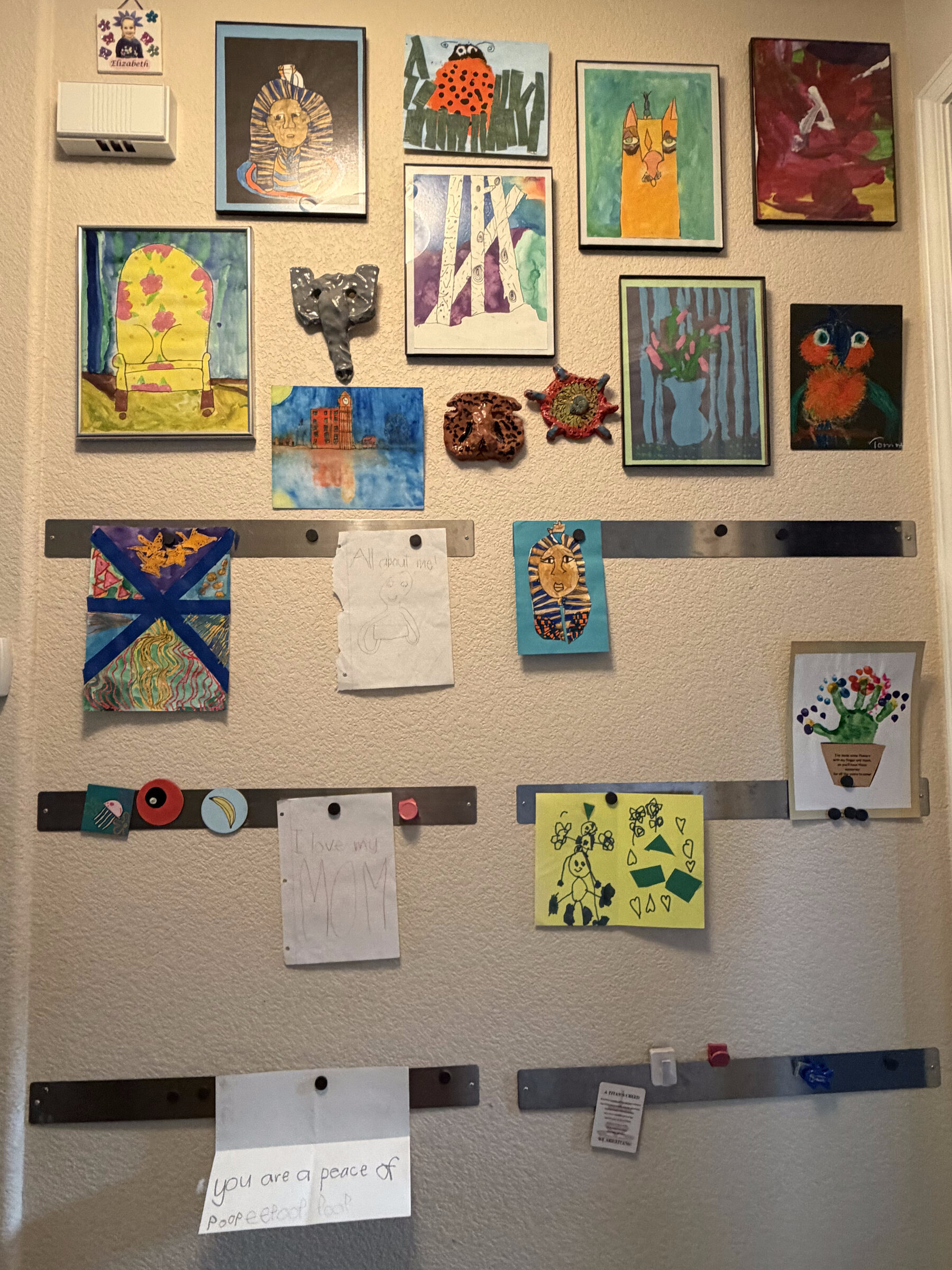 A hallway wall covered in a rotating gallery of kids' artwork, paintings, and pottery